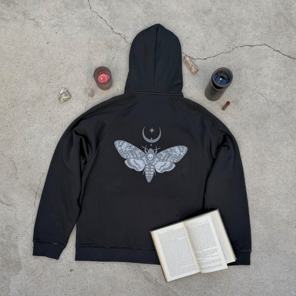 Black hoodie with moth design on a concrete surface with books and candles.