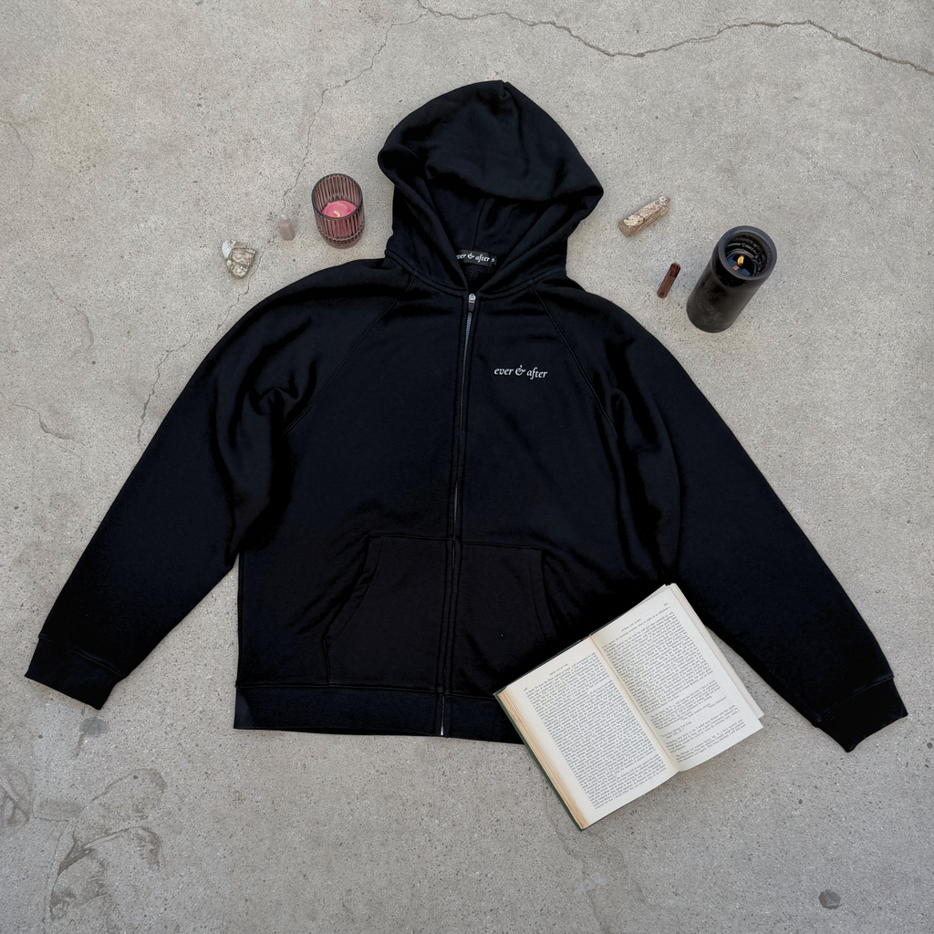 Black hoodie with a brand logo on a concrete surface with a book and other items.