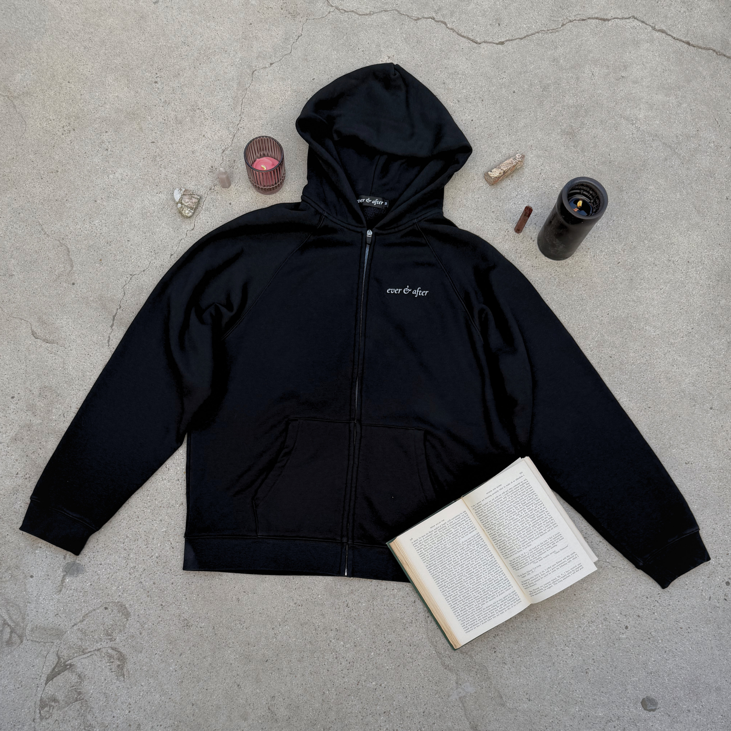 Black hoodie with a brand logo on a concrete surface with a book and other items.