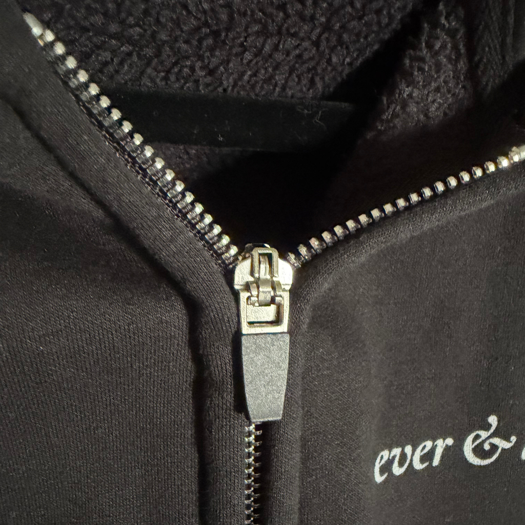 Close-up of a black hoodie with a zipper and 'ever & ever' embroidery.