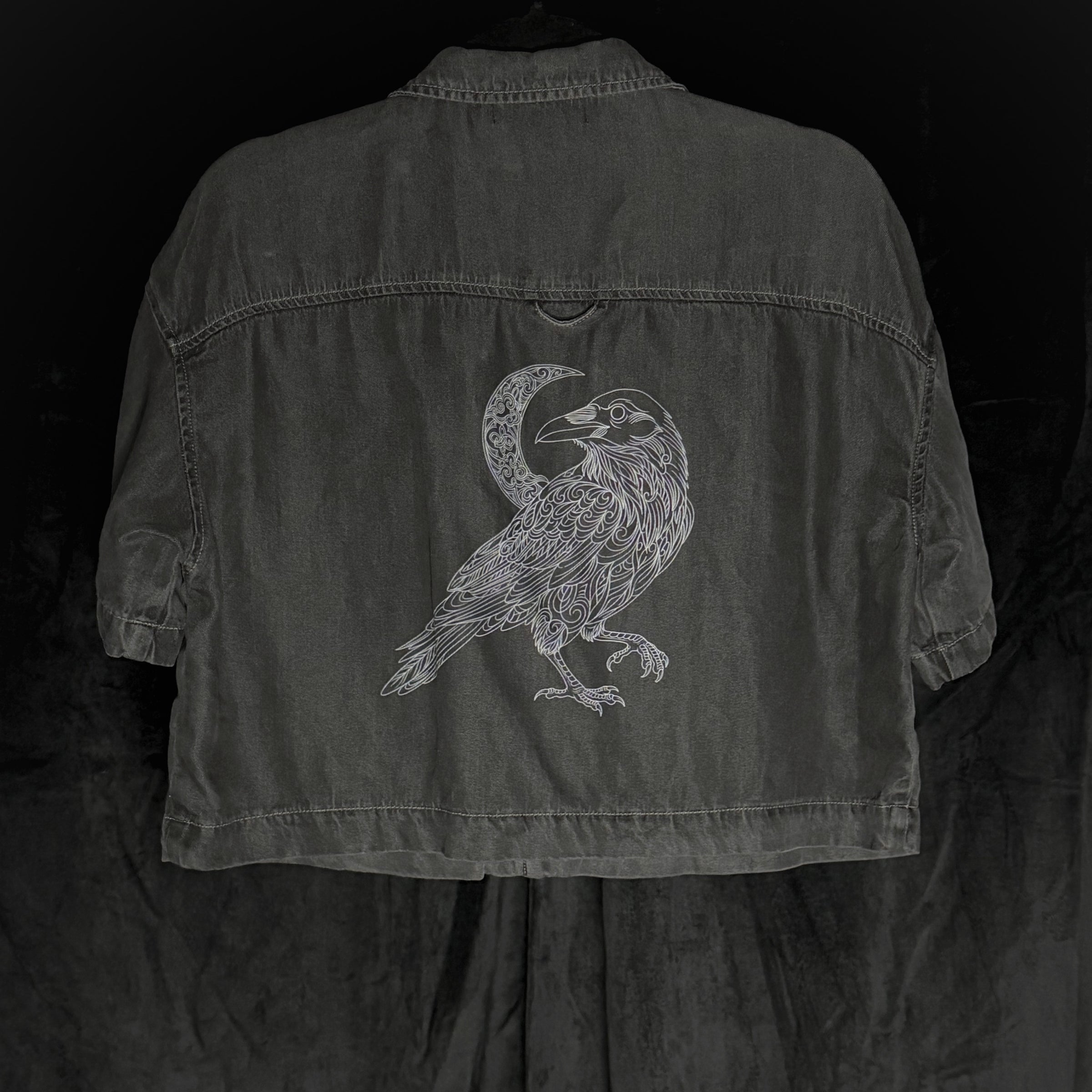 Dark denim jacket with a bird and moon design on the back against a black background