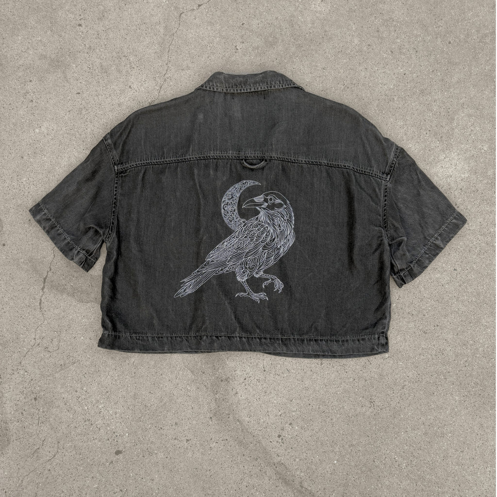 Black denim jacket with a bird and moon design on a concrete surface