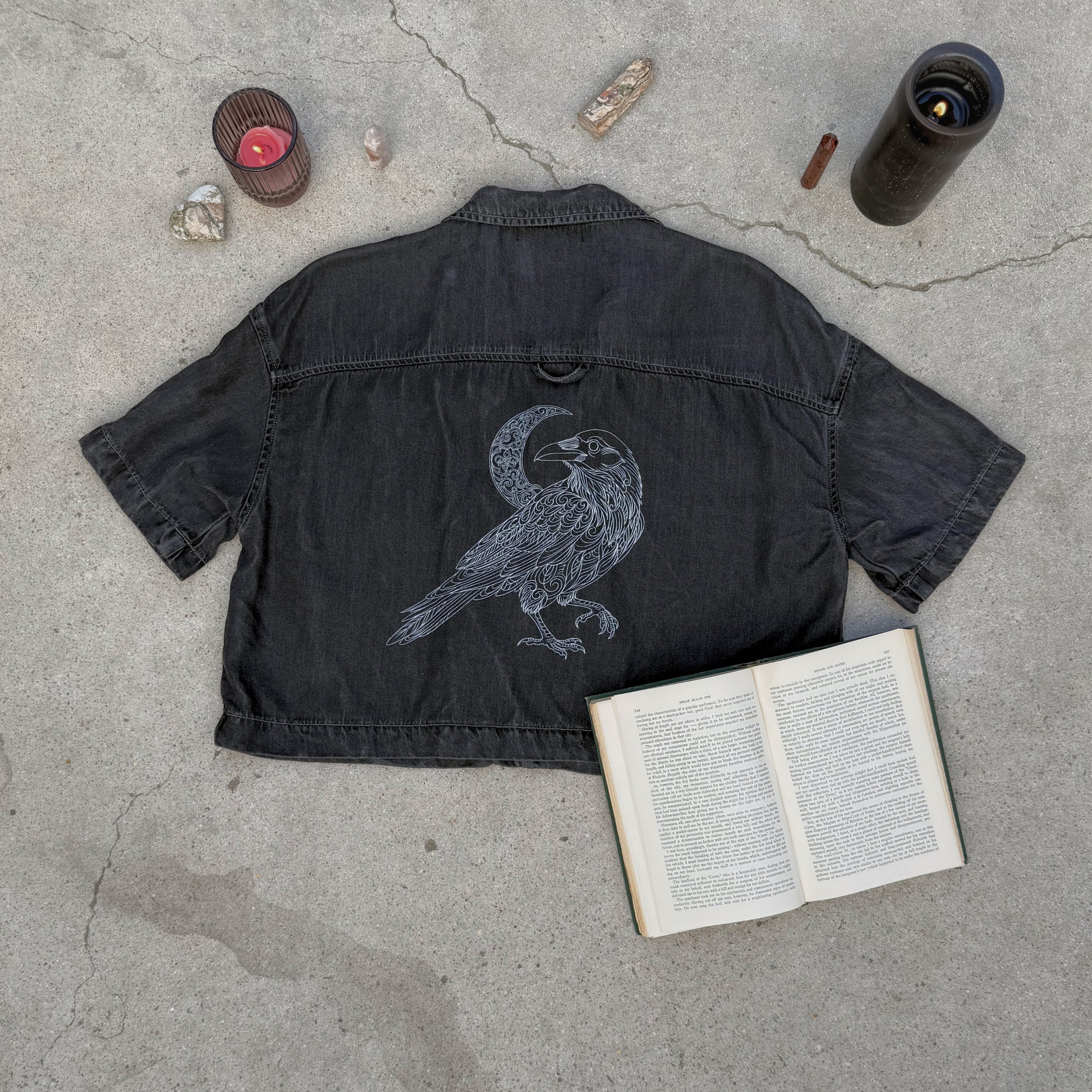 Black jacket with a bird design on a concrete surface with an open book and candles.