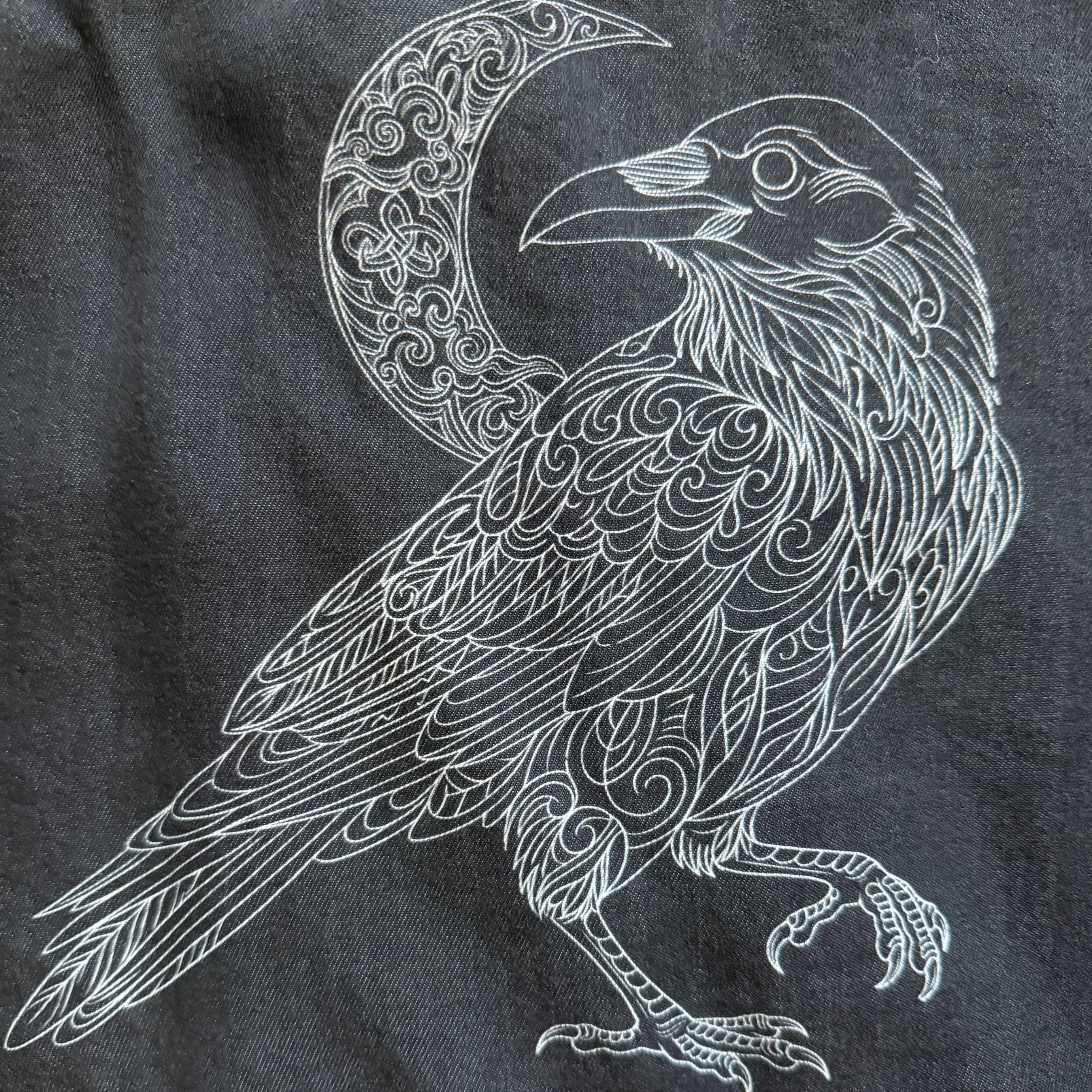 Decorative white crow design on a dark fabric background