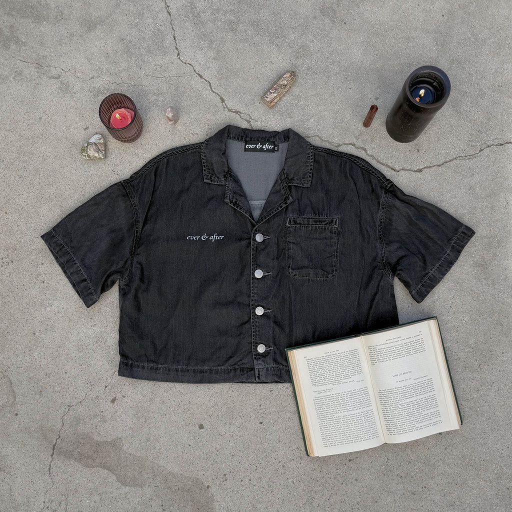 Black shirt with 'ever & after' branding on a concrete surface with an open book and candles.
