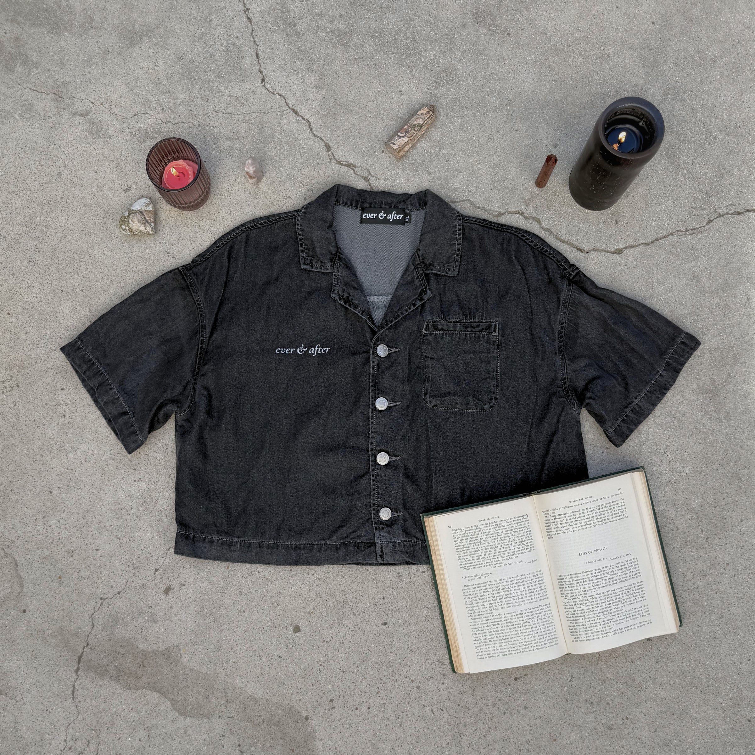 Black shirt with 'ever & after' branding on a concrete surface with an open book and candles.