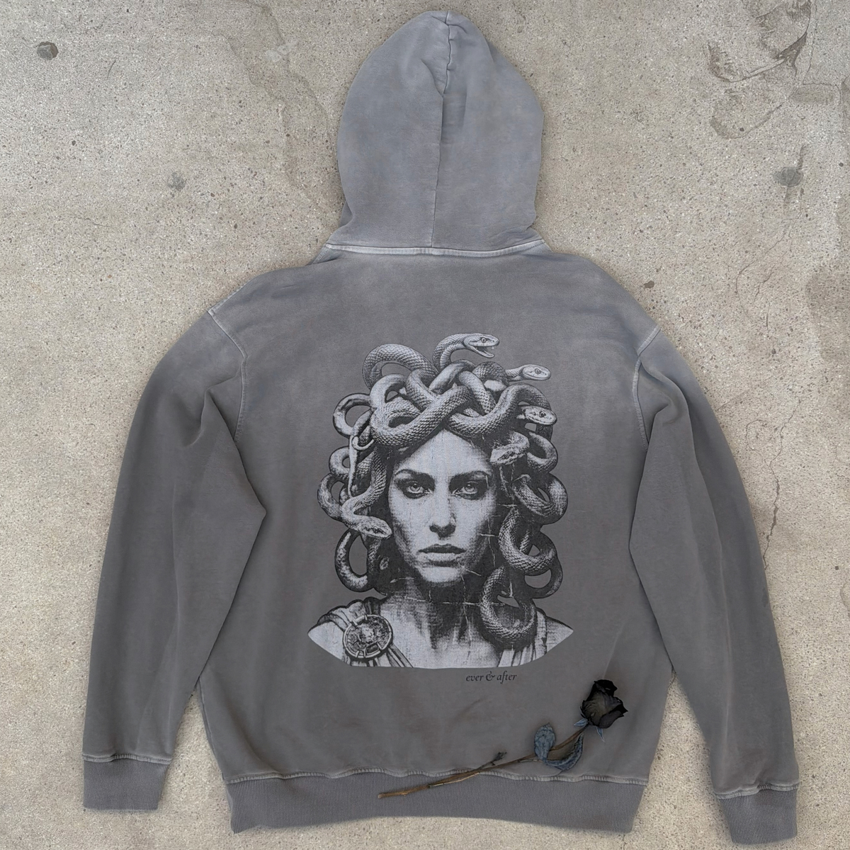 Gray hoodie with Medusa graphic on a concrete surface
